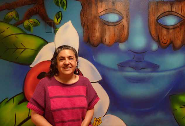Guisela Latorre sitting in front of the mural in the WGSS department suite, 286 University Hall