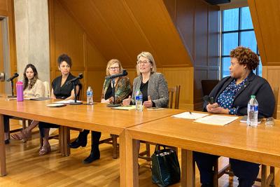 Five panelists sit at table and converse with each other