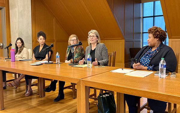 Five panelists sit at table and converse with each other