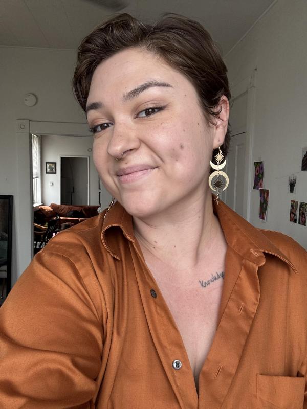 A selfie of Kayley DeLong, a white androgynous person, wearing an orange button down shirt. 