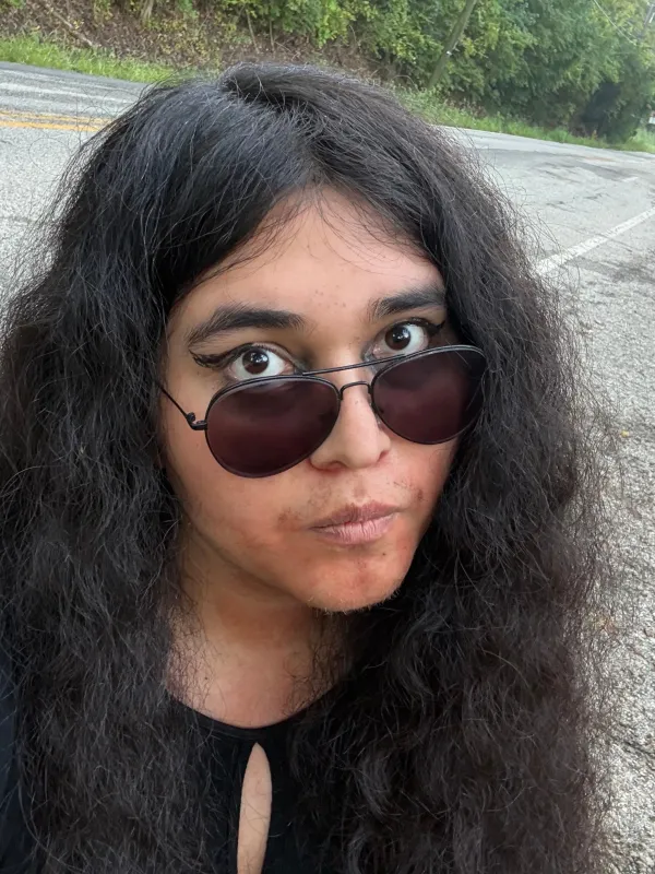 Marijane, a Latina transsexual woman with aviator sunglasses, eyeliner, and long black hair in a middle part.
