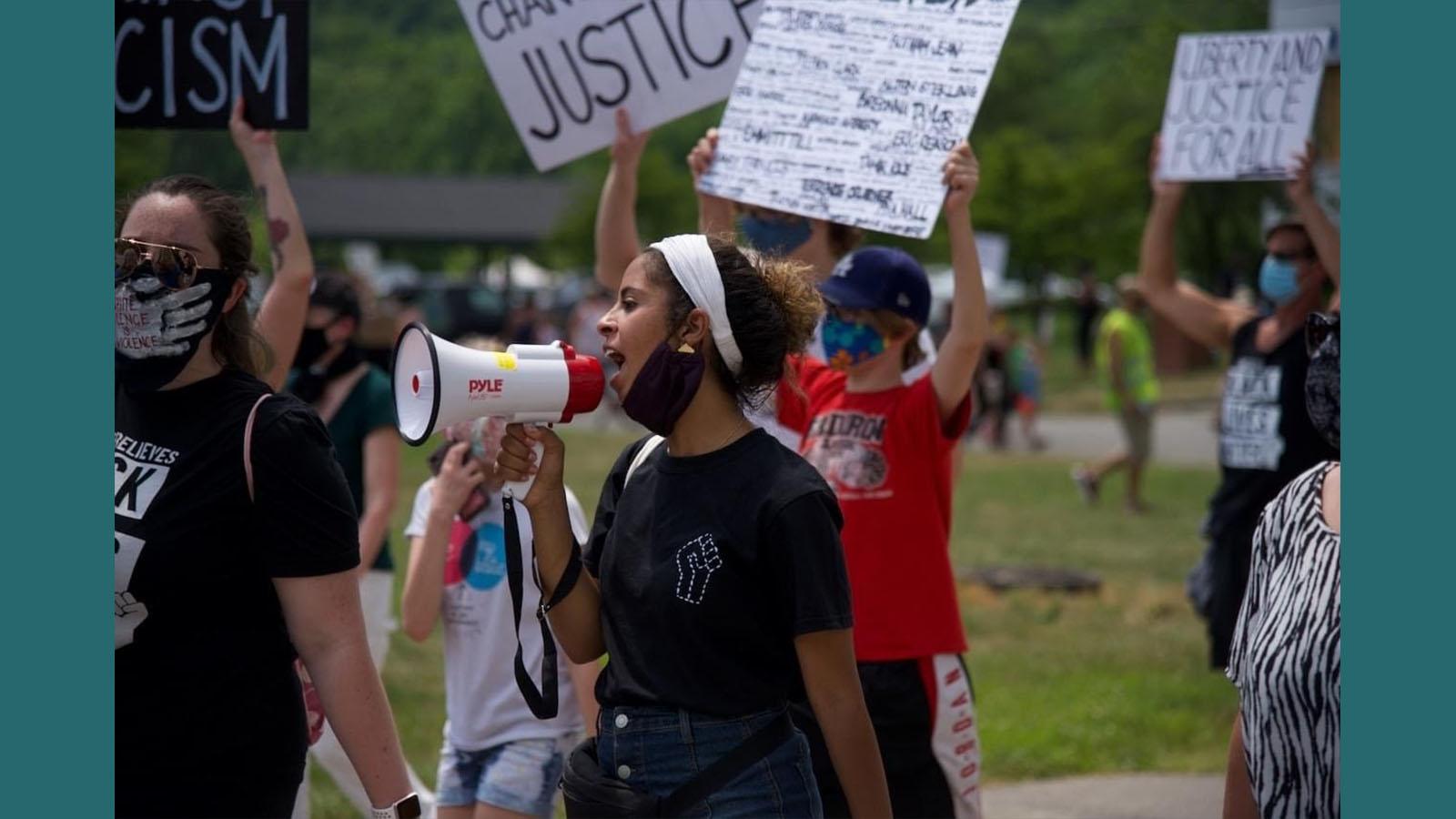 Black Lives Matter protester using a megaphone with other protesters holding signs in background